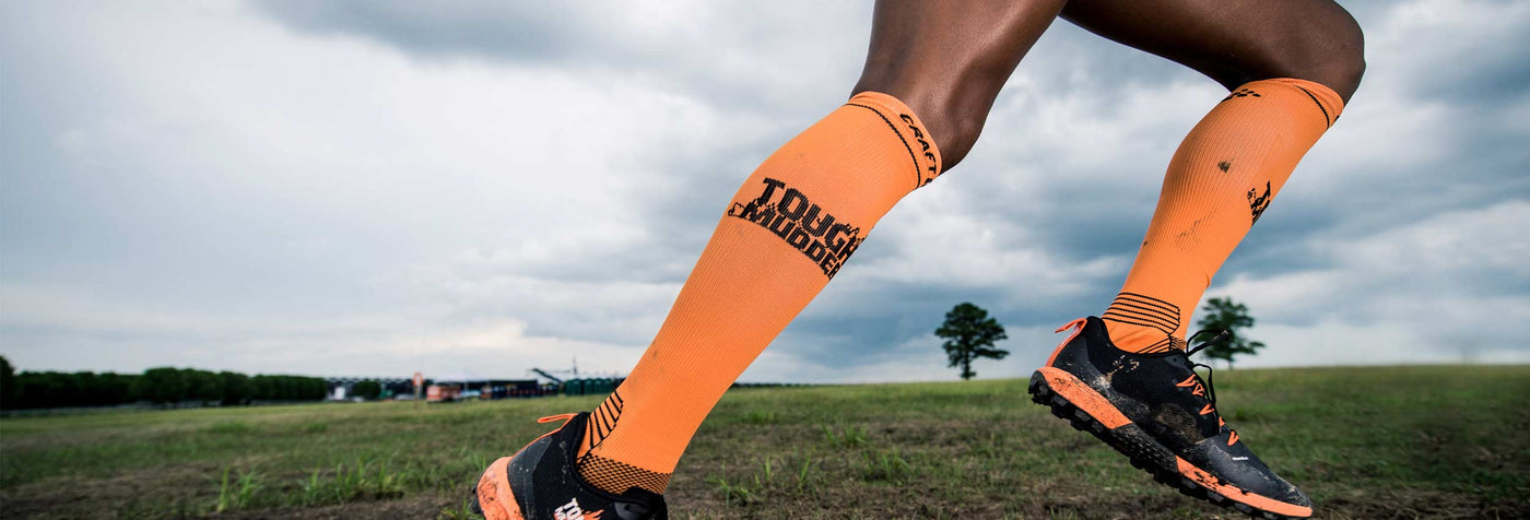 image of an tough mudder running wearing orange tough mudder by craft compression training socks