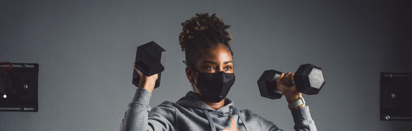Woman working out with dumbbells and wearing a Tough Mudder face mask